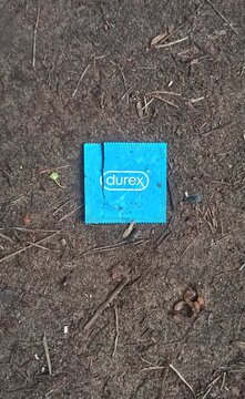 A blue Durex condom wrapper lying discarded on earthy ground outdoors, highlighting themes of littering, hygiene, and environmental awareness.