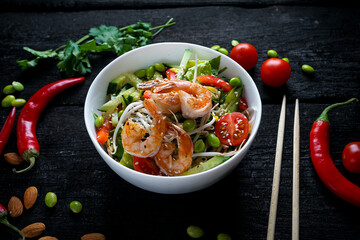 bibimbap with sprouts, shrimp, tomatoes, peppers, cucumbers and beans in a white plate on a dark background with decor
