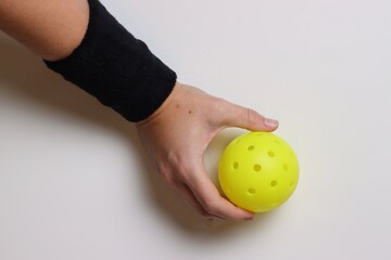 Woman holding a pickleball ball with a black wrist brace in a light background