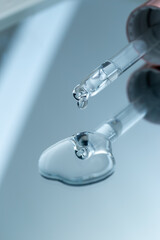 Close-up pipette with pure liquid face serum or essential oil with drop on mirror background for cosmetic ingredient concept.