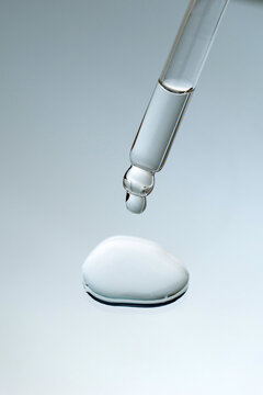 Close-up pipette with pure liquid face serum or essential oil with drop on gray background for cosmetic ingredient concept.