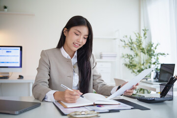 Smiling businesswoman analyzing documents and taking notes at her modern office desk.