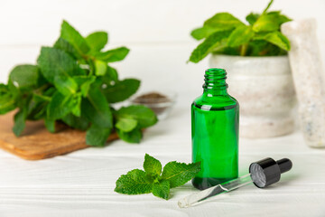 Essential oil mint on a wooden background. Peppermint essential oil with fresh mint leaves. A bottle of aromatherapy oil. Mint extract. The concept of natural cosmetics, spa care. copy space