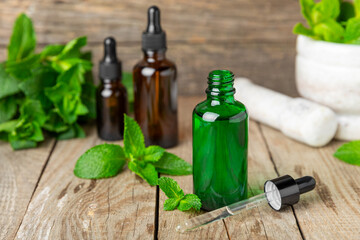 Essential oil mint on a wooden background. Peppermint essential oil with fresh mint leaves. A bottle of aromatherapy oil. Mint extract. The concept of natural cosmetics, spa care. copy space