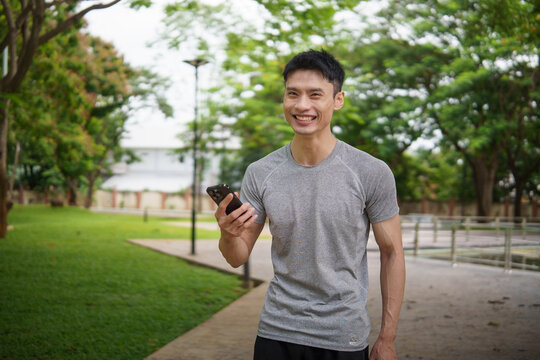 Smiling man in athletic wear holding smartphone while walking in a park. Healthy lifestyle concept.