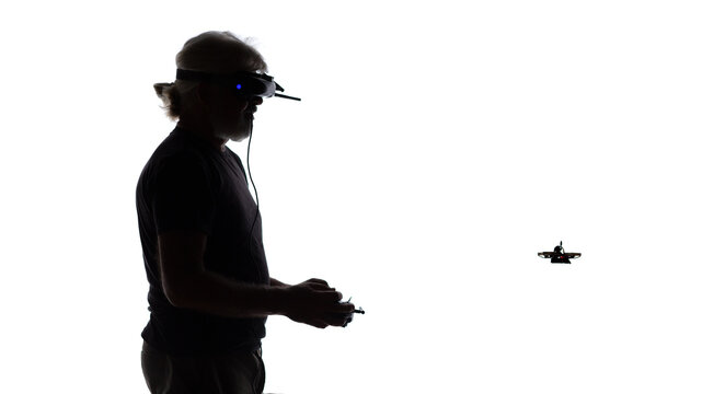 Silhouetted elderly man operating racing drone in goggles and remote control on a white isolated background, modern hobby and technology concept