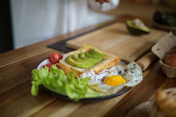 Healthy breakfast plate with avocado toast, sunny side up egg, and fresh vegetables on wooden table.