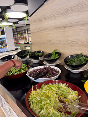 Fresh Mixed Greens Plates at All-Inclusive Buffet. Hands Selecting Greens at Hotel Salad Buffet