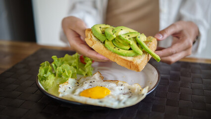 Healthy breakfast preparation with avocado toast, fried egg, and green vegetables.