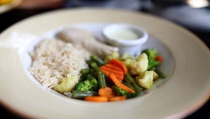 Vibrant platter of steamed vegetables and rice with a creamy dip served in a cozy dining setting