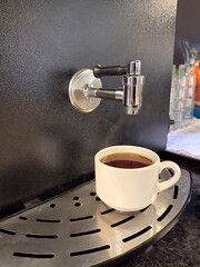 ceramic cup placed under automatic tea dispenser in self-service area. Image shows simple and fast way to get hot tea in cafes, offices, and public places