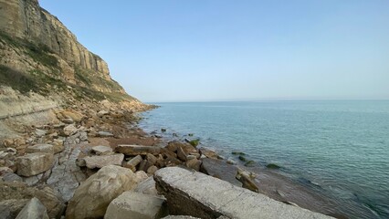 Rocky Coastal Cliffside with Calm Blue Sea Under Clear Sky- Hastings 