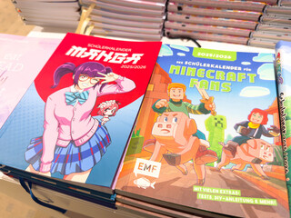 Naklejka premium Villach, Austria - August 05, 2025: Colorful manga and Minecraft themed school calendars displayed on a table, showcasing vibrant illustrations and engaging designs for students