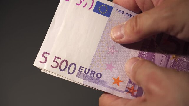 A hand counts 500 euro banknotes in preparation for a financial transaction