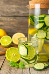 Cucumber water with lemon, lime and mint on a wooden table. Water infused with sliced ​​cucumber in a drinking glass. Tonic refreshing drink. Cucumber lemonade.Summer natural cooling drink.Copy space