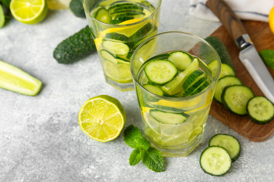Cucumber water with lemon, lime and mint on a wooden table. Water infused with sliced ​​cucumber in a drinking glass. Tonic refreshing drink. Cucumber lemonade.Summer natural cooling drink.Copy space