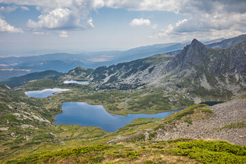 Seven Rila Lakes, a group of glacial lakes located in the Rila Mountains of Bulgaria, a highly popular natural attraction. Glacial lake cirque nestled in mountain under a cloudy summer sky.