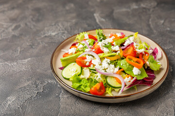 Cucumber salad on a wooden background.Homemade salad with fresh vegetables, cucumber, tomato, sweet pepper and lettuce in a plate.Vegetarian spring salad.Vegetarian diet.Healthy eating.Space for text