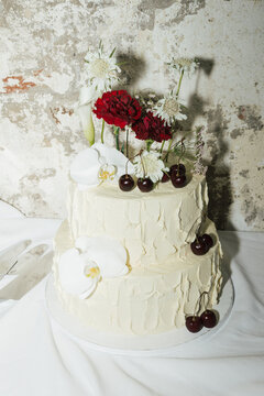 modern white wedding cake with roses and cherries on top, photographed with flash