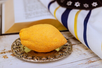 Traditional Jewish etrog citrus fruit displayed on open prayer book prayer shawl with Star of David pattern during Sukkot holiday ritual.