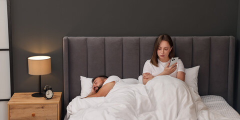 Betrayal. Jealous woman finding proofs of her unfaithful husband on smartphone while he sleeping in...