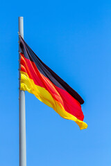 Flag of Germany waving in the wind against the blue sky background.