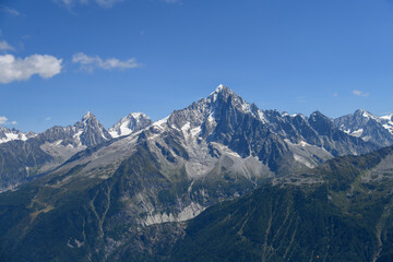 Stunning mountain range near Chamonix in the French Alps under clear blue sky. Jagged peaks, rocky ridges, and lush alpine slopes create a dramatic high-altitude landscape.