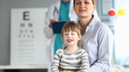Mother and daughter enjoy a cheerful moment during an eye exam in a friendly, well-lit clinic environment