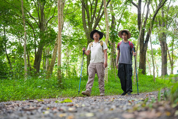Fototapeta premium Adventurous man and grandson hiking with trekking poles through a scenic woodland trail, Men exploring nature, enjoying a sunny day trekking on a dirt path in a lush green forest