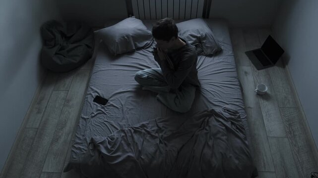 Sadness and pain after breakup. Young man sitting on bed holding photo of ex girlfriend, hugging it tightly, feeling deep pain and loneliness.