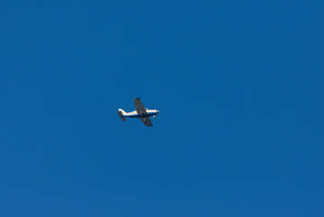 A small, blue and white propeller plane is flying high in a clear, blue sky on a bright day.