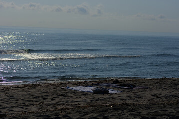 Two towels and a pair of shoes are seen left on a sandy beach next to the calm sea on a sunny day.