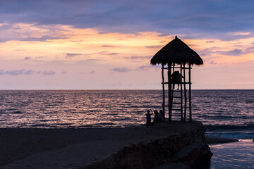 Hut lookout tower at sunset in Puerto Vallarta Mexico with silhouette of people and a cloudy sky