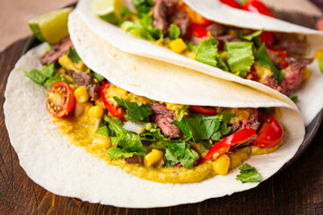 Mexican tacos, tortilla with beef, vegetable sauce, corn and tomatoes on the table close up