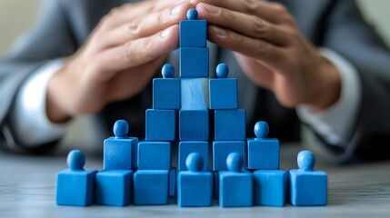 Blue Wooden Figure Pyramid Protected by Hands Representing Hierarchy, Leadership, and Teamwork