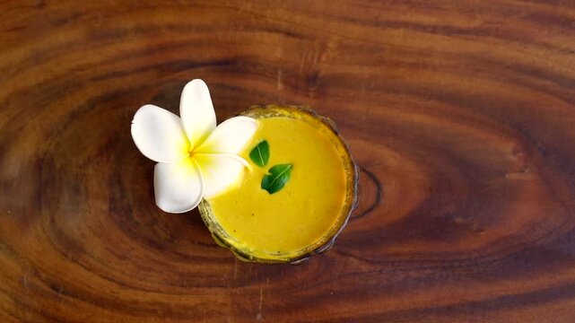 Closeup homemade ubtan facial in bowl with a big white champa flower. Ayurvedic face pack of Haldi (Turmeric), Rose water and gram flour. Natural beauty and skincare using since ancient India