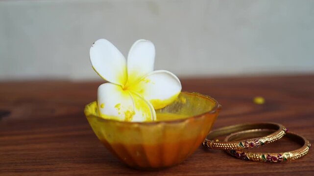 Closeup homemade ubtan facial in bowl with a big white champa flower. Ayurvedic face pack of Haldi (Turmeric), Rose water and gram flour. Natural beauty and skincare using since ancient India