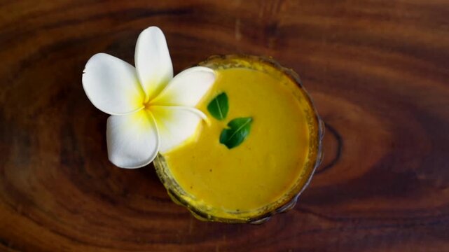 Closeup homemade ubtan facial in bowl with a big white champa flower. Ayurvedic face pack of Haldi (Turmeric), Rose water and gram flour. Natural beauty and skincare using since ancient India