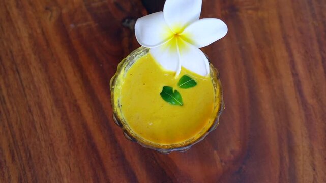 Closeup homemade ubtan facial in bowl with a big white champa flower. Ayurvedic face pack of Haldi (Turmeric), Rose water and gram flour. Natural beauty and skincare using since ancient India