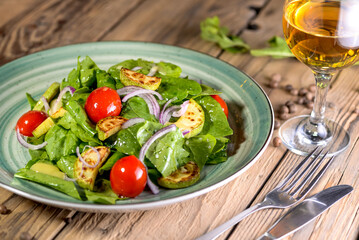 salad with greens, tomatoes and zucchini in a green plate on a background with wine