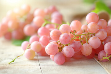 Close-up of fresh pink grapes on a light wooden table in bright high-key natural light, showing translucent rosy skin and smooth clusters in a clean kitchen setting.