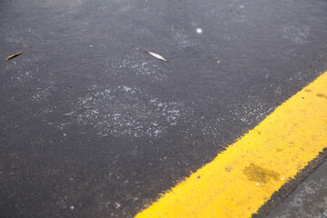 Icy pavement covered with a thin layer of freezing rain, featuring a bright yellow line, creating a stark contrast with the dark asphalt surface and enhancing winter ambiance