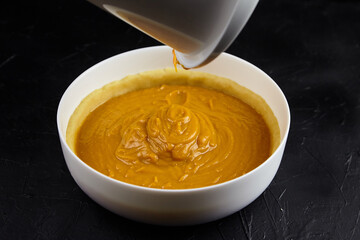 Pumpkin pie filling being poured into a crust in a white bowl, showcasing the creamy texture and rich color, perfect for autumn baking and festive celebrations