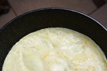 Omelette cooking in a non-stick frying pan, showcasing a creamy texture and golden edges, with a warm kitchen ambiance enhancing the culinary experience