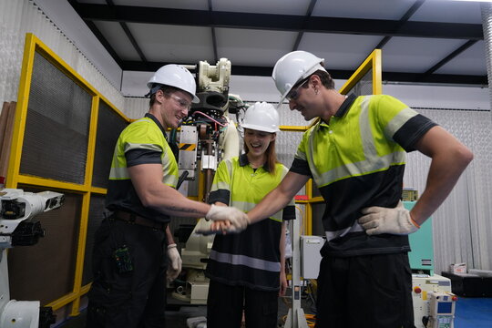 team of male and female engineers join hands and happily repair a remote control circuit board to set the working command of a robot arm in a factory to determine the production line in the factory.
