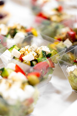Close-up of fresh Greek salad in plastic containers with cucumbers, tomatoes, feta cheese, olives, and herbs. Bright, healthy, and ready to serve.
