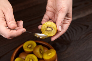 Close-up of hands holding a sliced golden kiwi fruit with a spoon, showcasing its unique texture and vibrant color, emphasizing healthy eating and fresh produce