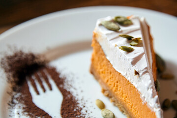 Delicious slice of pumpkin cheesecake topped with whipped cream and pumpkin seeds, beautifully presented on a white plate with cocoa powder art, showcasing culinary creativity and dessert aesthetics