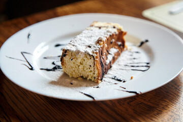 Delicious slice of chocolate cake topped with powdered sugar and drizzled with chocolate sauce, served on a white plate, showcasing a tempting dessert experience