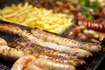 Grilled sausages sizzling on a barbecue grill, surrounded by crispy fries and various meats, creating a delicious and inviting outdoor dining atmosphere